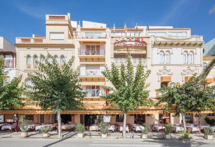 Facade of Hotel Los Globos, a gay-friendly hotel. Outdoor dining area with tables and chairs. Balconies and awnings. Travel destination.