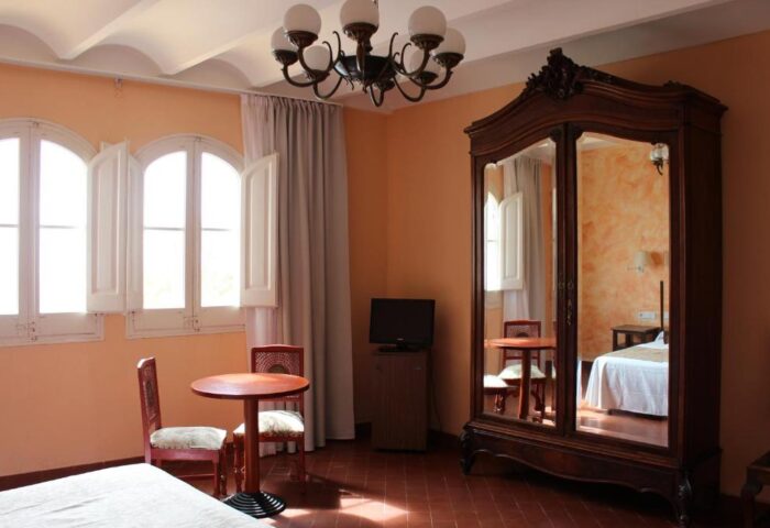 Hotel Los Globos gay-friendly hotel room. It features a wardrobe with mirrors, a table with chairs, and a chandelier.