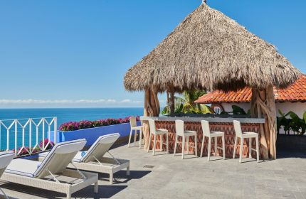 Hotel Luxury Patio Azul's gay-friendly rooftop bar with ocean view. Thatched roof, bar stools, and lounge chairs create a relaxing vibe.