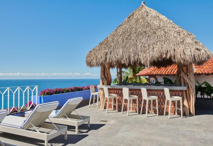 Hotel Luxury Patio Azul's gay-friendly rooftop bar with ocean view. Thatched roof, bar stools, and lounge chairs create a relaxing vibe.