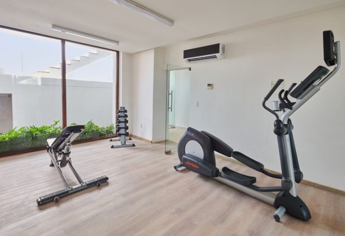 Hotel Luxury Patio Azul's gym. Gay-friendly hotel features fitness equipment: elliptical machine, weight bench, and dumbbells. Modern, clean space.