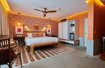 Hotel Luxury Patio Azul's gay-friendly room. A king bed with a bench, patterned wallpaper, and a ceiling fan create a warm ambiance.