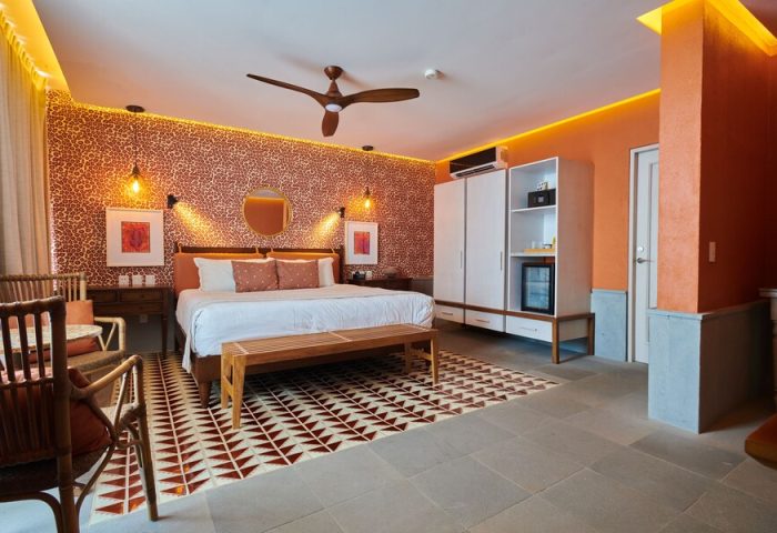 Hotel Luxury Patio Azul's gay-friendly room. A king bed with a bench, patterned wallpaper, and a ceiling fan create a warm ambiance.