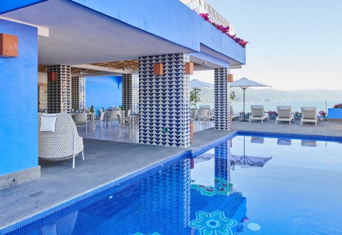 Hotel Luxury Patio Azul's gay-friendly appeal: poolside view of the patio, dining area, lounge chairs, and ocean. A vibrant, relaxing space.