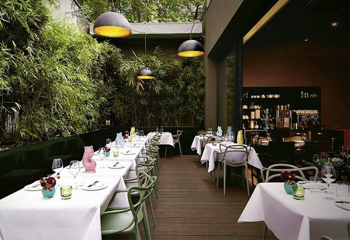 Hotel MANI by AMANO's garden restaurant. Tables with white tablecloths and green chairs. Lush green bamboo backdrop. Gay-friendly hotel.
