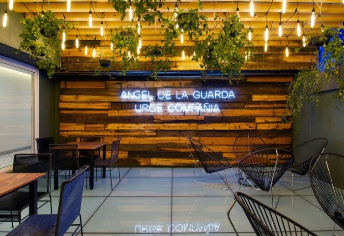 Hotel MX mas reforma gay-friendly hotel interior. Angel de la Guarda Urge Compania neon sign, plants, and modern seating area.