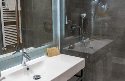 Hotel Madeira Centro gay-friendly bathroom. White sink, shower with glass partition, and grey tiles. Modern design for gay travelers.