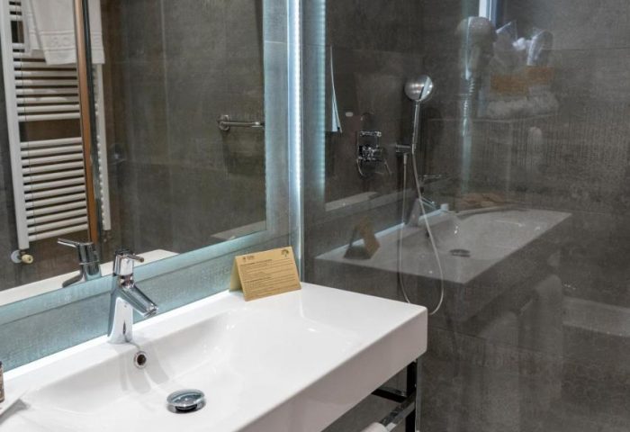 Hotel Madeira Centro gay-friendly bathroom. White sink, shower with glass partition, and grey tiles. Modern design for gay travelers.