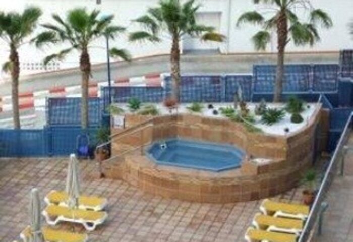 Hotel Madeira Centro's gay-friendly outdoor pool area. Palm trees, lounge chairs, and a jacuzzi tub create a relaxing atmosphere.