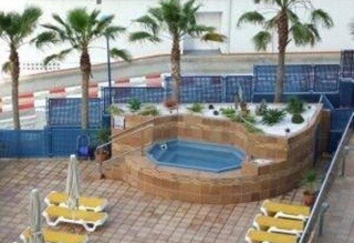 Hotel Madeira Centro's gay-friendly outdoor pool area. Palm trees, lounge chairs, and a jacuzzi tub create a relaxing atmosphere.
