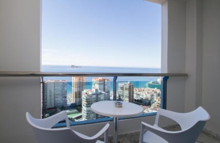 Balcony view at gay-friendly Hotel Madeira Centro. Table and chairs overlooking Benidorm's skyline and the Mediterranean sea. Relaxing travel.