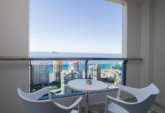 Balcony view at gay-friendly Hotel Madeira Centro. Table and chairs overlooking Benidorm's skyline and the Mediterranean sea. Relaxing travel.