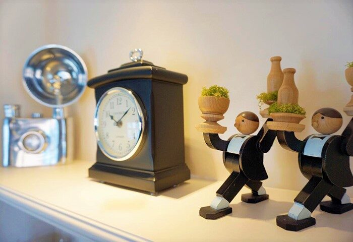 Hotel Madera Hollywood decor: Clock, vintage camera, and wooden butler figures holding plants. Gay-friendly hotel room detail.