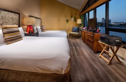 Hotel Maya A Doubletree Hotel guest room with two beds, waterfront view, TV, luggage, and modern decor. A gay-friendly hotel.