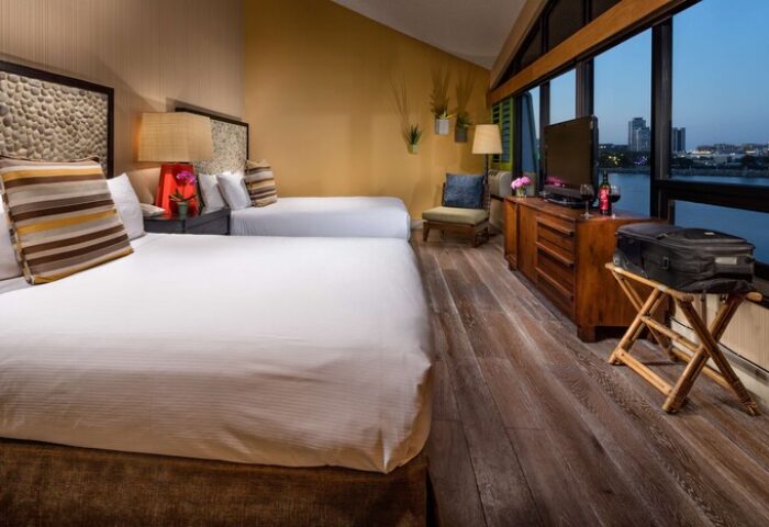 Hotel Maya A Doubletree Hotel guest room with two beds, waterfront view, TV, luggage, and modern decor. A gay-friendly hotel.