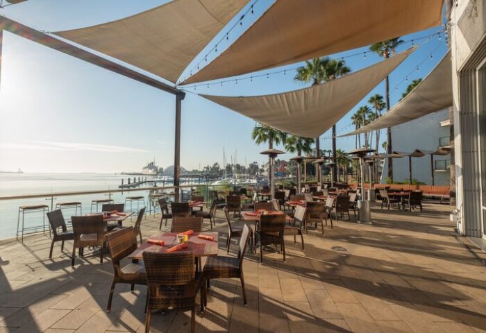 Outdoor dining area at Hotel Maya A Doubletree Hotel, a gay-friendly hotel. Tables and chairs under sunshades, with ocean views.