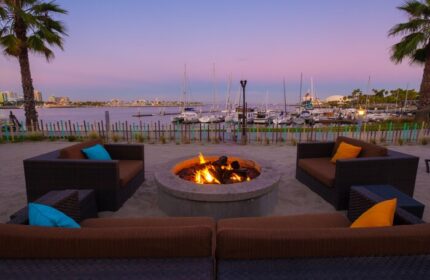 Hotel Maya A Doubletree Hotel's gay-friendly fire pit lounge area at dusk. Waterfront view, boats, palm trees, and cozy seating.
