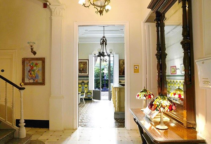 Hotel Medium Renaixenca's interior. Lobby with vintage lamps, mirror, and staircase. Gay-friendly hotel with unique design elements.