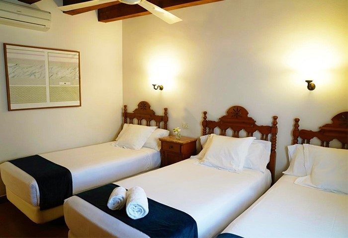 Hotel Medium Renaixenca gay-friendly hotel room with three beds. Comfortable stay for gay travelers. Room features wooden headboards, and soft lighting.