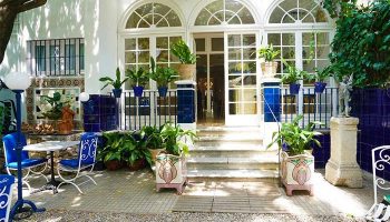 Hotel Medium Romantic gay-friendly hotel entrance. White facade, arched windows, blue accents, plants. Welcoming, stylish, romantic.