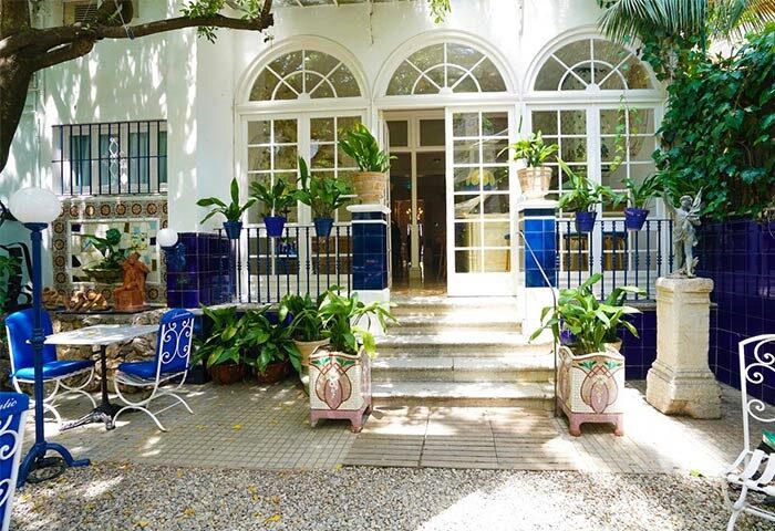 Hotel Medium Romantic gay-friendly hotel entrance. White facade, arched windows, blue accents, plants. Welcoming, stylish, romantic.