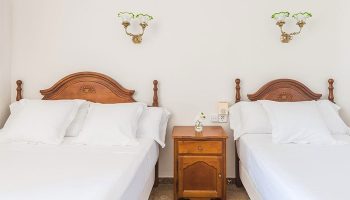 Hotel Medium Romantic gay-friendly room. Two beds with white linens, wooden headboards, and a nightstand. Ideal for gay travel.