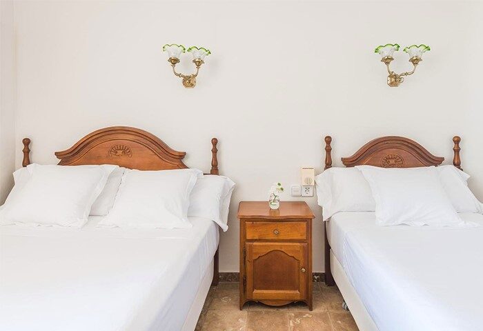Hotel Medium Romantic gay-friendly room. Two beds with white linens, wooden headboards, and a nightstand. Ideal for gay travel.