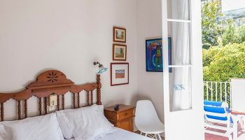 Hotel Medium Romantic gay-friendly room. Bedroom with wooden headboard, bedside table, chair, and balcony with sunbeds. Travel advice.