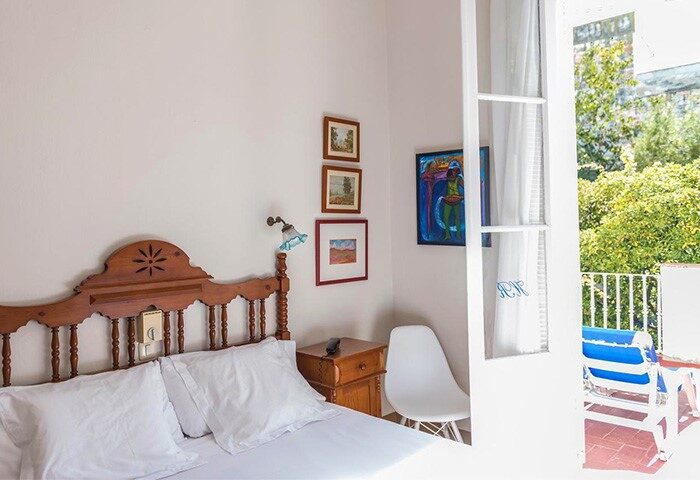 Hotel Medium Romantic gay-friendly room. Bedroom with wooden headboard, bedside table, chair, and balcony with sunbeds. Travel advice.
