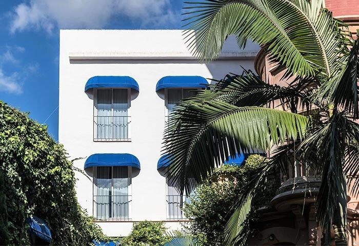 Hotel Medium Sitges Park facade. Gay-friendly hotel with blue awnings, balconies, and lush greenery. A welcoming spot for gay travelers.