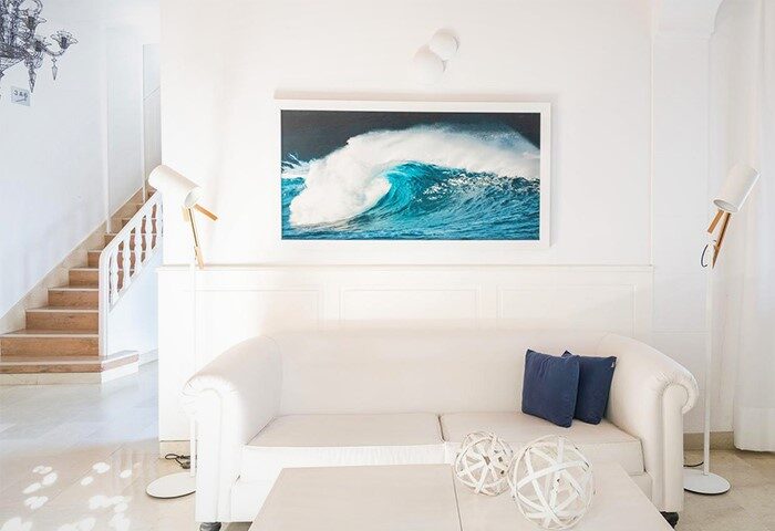 Hotel Medium Sitges Park's gay-friendly interior. White sofa with blue pillows, wave art, and modern lamps. Relaxing space.