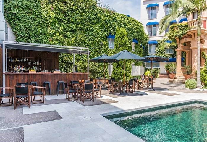 Hotel Medium Sitges Park gay-friendly hotel pool and bar area. Outdoor tables with umbrellas, bar, and building with greenery.