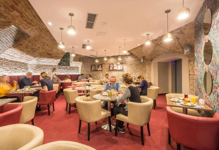 Hotel Memories Budapest's breakfast area. Guests enjoy their morning meal in the gay-friendly hotel's stylish dining room. Brick walls, warm lighting.