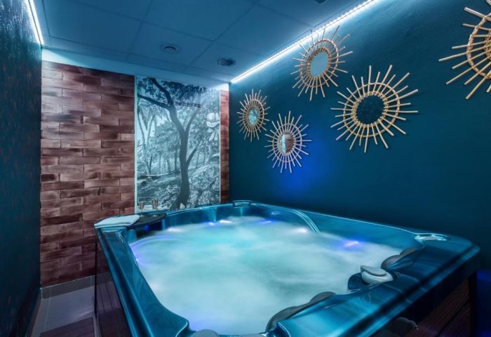 Hotel Memories Budapest gay-friendly hotel spa. Jacuzzi with blue lighting, sunburst mirrors, wood wall, and forest mural. Relaxing gay travel.