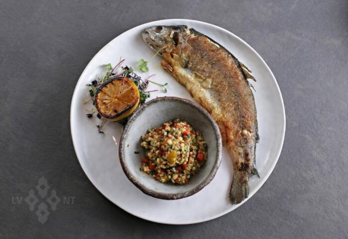 Fine dining at Hotel Memories Budapest, a gay-friendly hotel. Grilled fish, lemon, and a side dish are served on a white plate.
