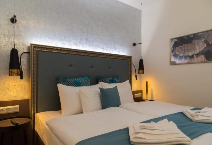 Hotel Memories Budapest gay-friendly hotel room. Twin beds with white linens, blue accents, and modern lamps. Comfortable stay in Budapest.