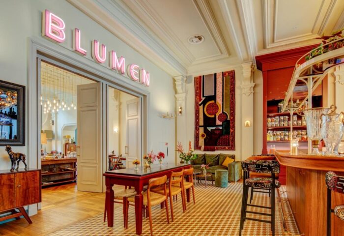 Hotel Mercier interior. Blumen neon sign above doorway, bar area, seating, and colorful decor. Gay-friendly hotel design.