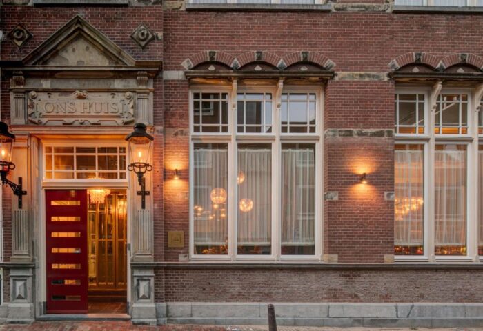Hotel Mercier, a gay-friendly hotel. Exterior view of the red brick building with a red door and white framed windows. Amsterdam travel.