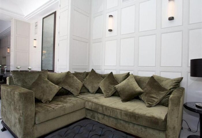 Lounge area at Hotel MiM Ibiza Es Vive, an adults-only, gay-friendly hotel. Olive green sofa with throw pillows against a white paneled wall.