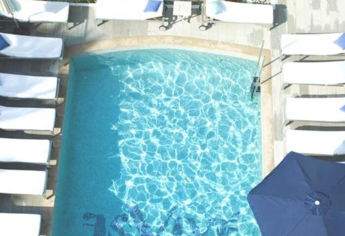 Hotel MiM Ibiza Es Vive Adults Only pool view. Gay-friendly hotel with sunbeds and blue umbrella, perfect for gay travel and relaxation.