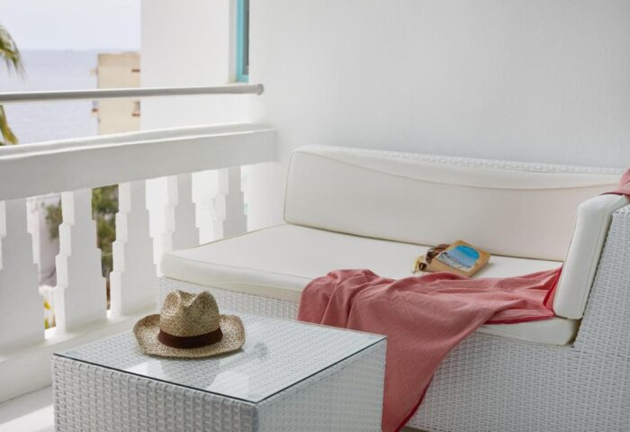 Hotel MiM Ibiza Es Vive Adults Only balcony. White wicker furniture with hat, book, and pink towel. Gay-friendly hotel detail.