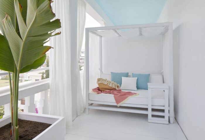 Balcony at Hotel MiM Ibiza Es Vive, an adults-only, gay-friendly hotel. White daybed with blue pillows, plant, and curtains.
