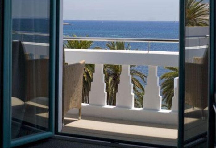 Hotel MiM Ibiza Es Vive Adults Only balcony view. Gay-friendly hotel room overlooking the sea. Palm trees add to the island's charm.