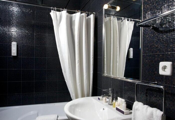Hotel MiM Ibiza Es Vive Adults Only bathroom. Stylish black tiled walls, white sink, tub, shower curtain, and mirror. Gay-friendly hotel.