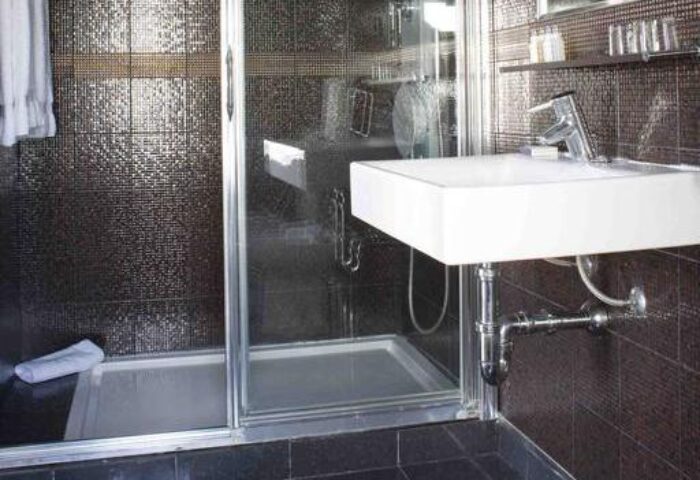 Bathroom at Hotel MiM Ibiza Es Vive, adults only, a gay-friendly hotel. Features a modern sink, shower with dark mosaic tiles, and sleek design.