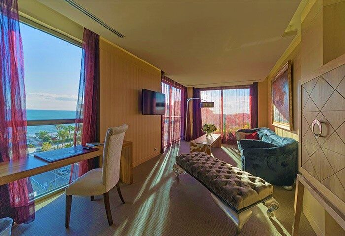 Hotel MiM Sitges gay-friendly room. Interior view of a luxurious suite with a desk, sofa, and ocean view. Gay travel in Sitges.