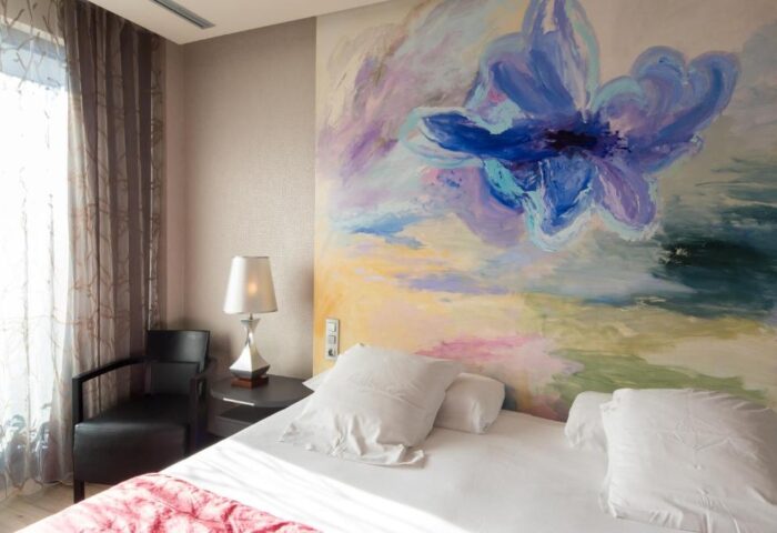 Hotel MiM Sitges gay-friendly room. Bed with white linens, floral mural, chair, and lamp. A comfortable stay for gay travelers.