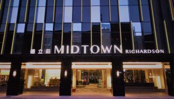 Facade of Hotel Midtown Richardson, a gay-friendly hotel. Modern architecture with glass windows and illuminated signage. Welcoming entrance.