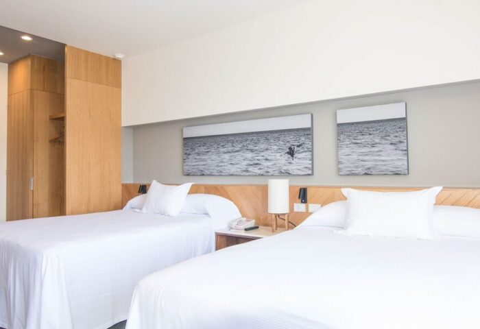 Hotel Mio Vallarta Adults Only room. Gay-friendly hotel featuring two beds with white linens and ocean-themed art. Modern, clean design.