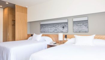 Hotel Mio Vallarta Adults Only room. Gay-friendly hotel featuring two beds with white linens and ocean-themed art. Modern, clean design.